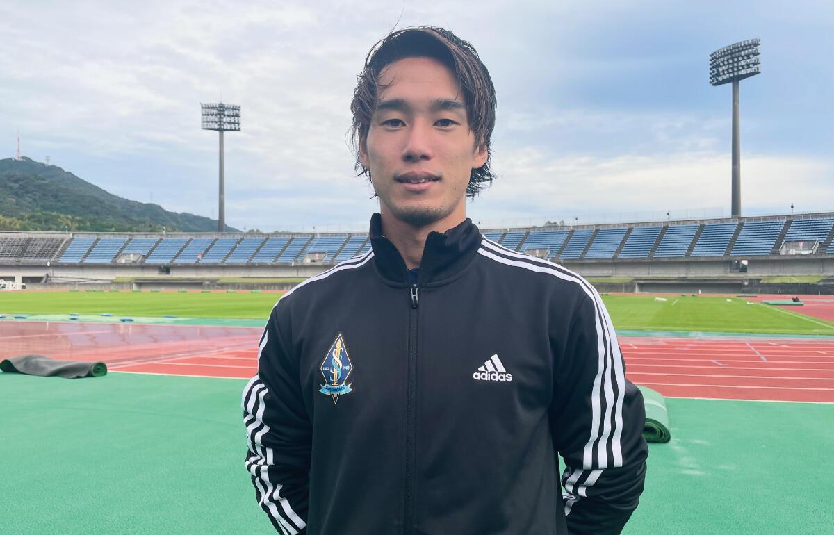 ソニー仙台FCの平田健人選手が、青と白の13番のユニフォーム姿で芝生のピッチを走る。クラブの活動終了を前に、試合に臨む彼の真剣な眼差しが印象的だ。